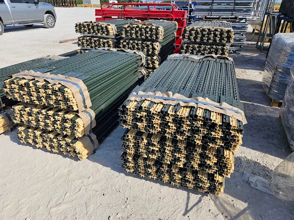 Bundled green painted and galvanized studded steel T posts strapped on pallets at a farm fence supply yard