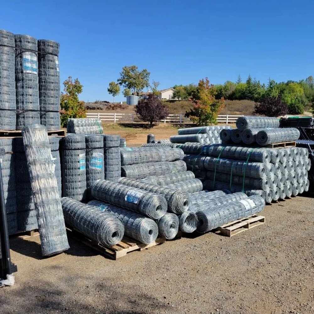 Bulk rolls of galvanized hinge joint field fence stacked on pallets for wholesale supply